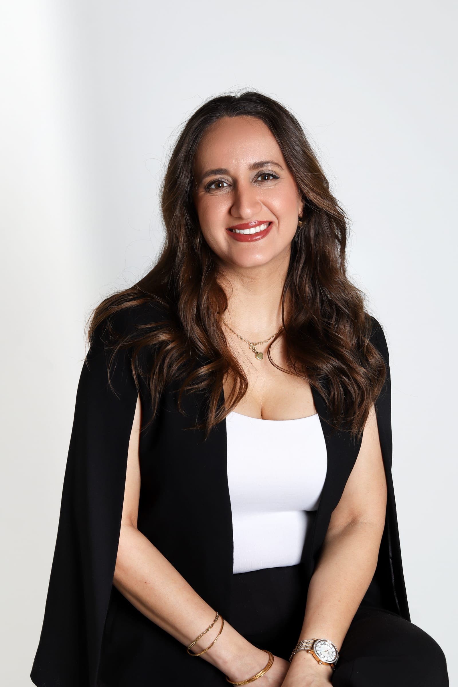 Aya in a black cape blazer and white top, seated and smiling at the camera