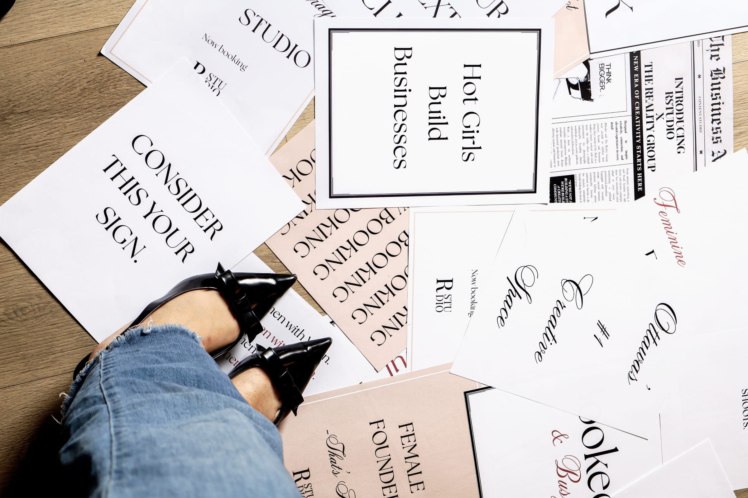 Printed cards and a "Hot Girls Build Businesses" sign laid out on the floor beside black pointed heels