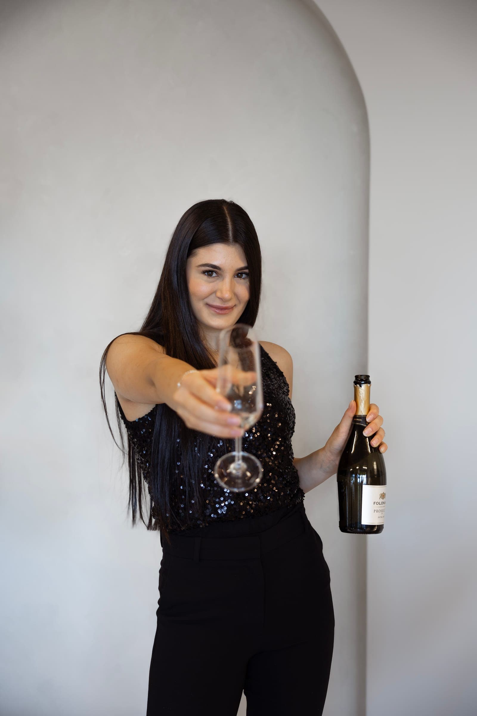 An agent in a sequin top holding out a champagne flute and a bottle of champagne