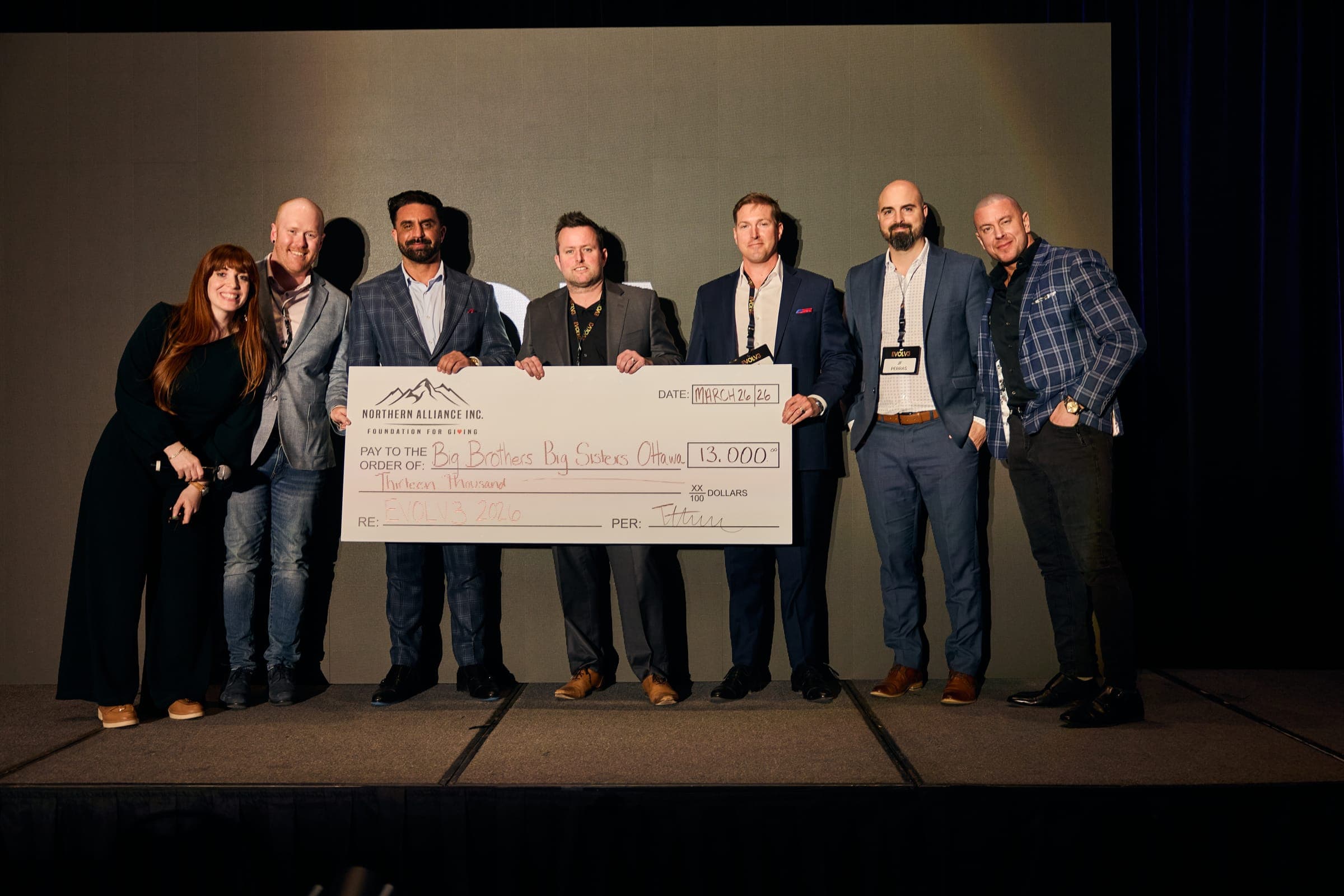 A group on stage holding an oversized charity cheque at a Northern Alliance event