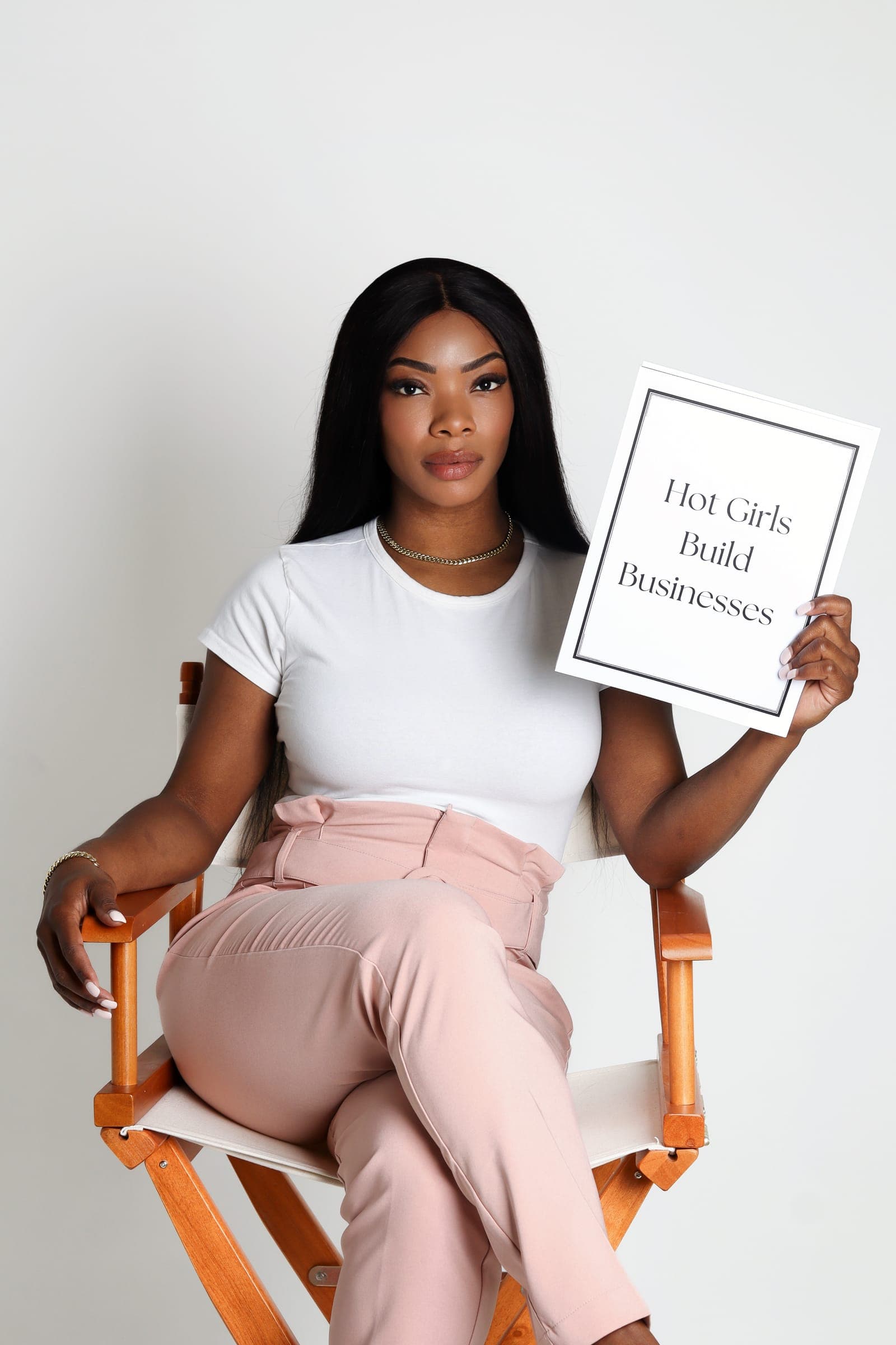 An agent seated in a director's chair holding a "Hot Girls Build Businesses" card