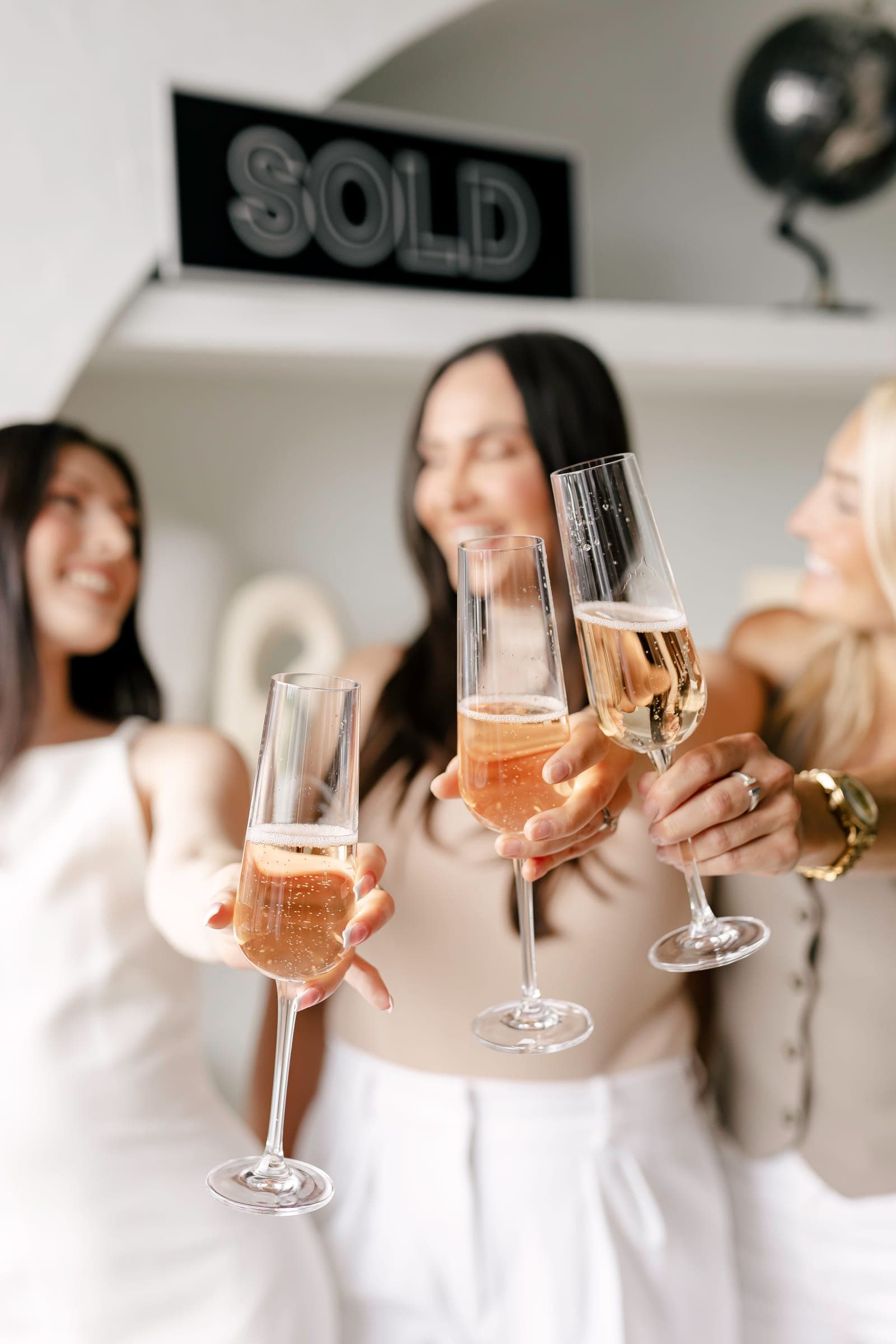 Agents raising champagne flutes in front of a "SOLD" sign