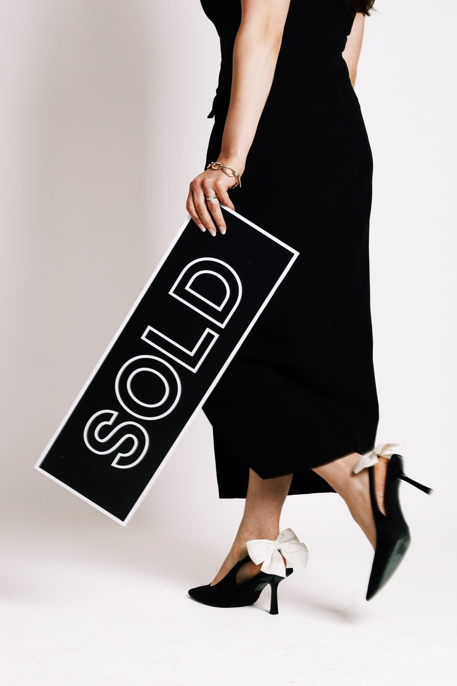 An agent in a long black skirt and heels carrying a "SOLD" sign