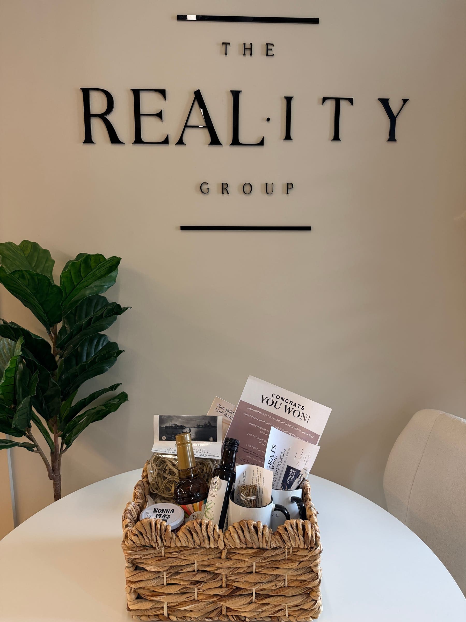 A wicker gift basket on a white table in front of The Reality Group wall sign