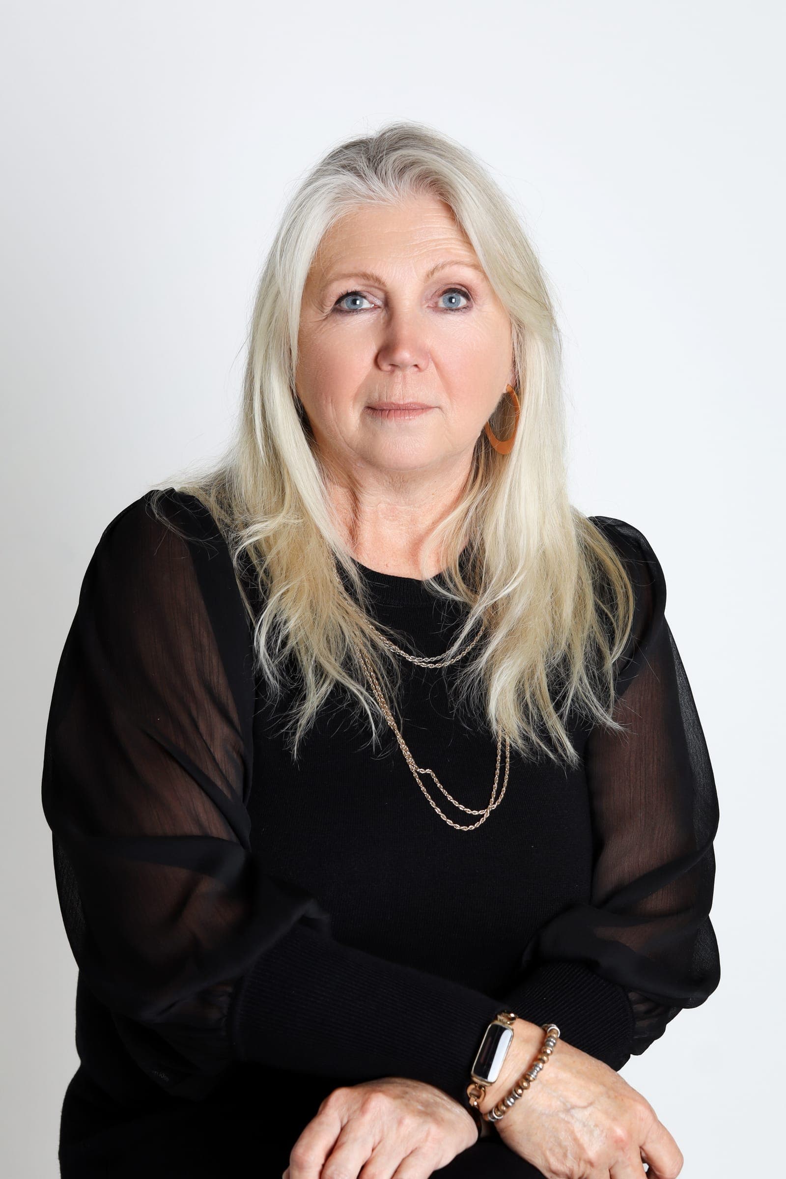 Gail Sala, our In-House Stager and Interior Design Specialist, in a black top with sheer sleeves against a white backdrop