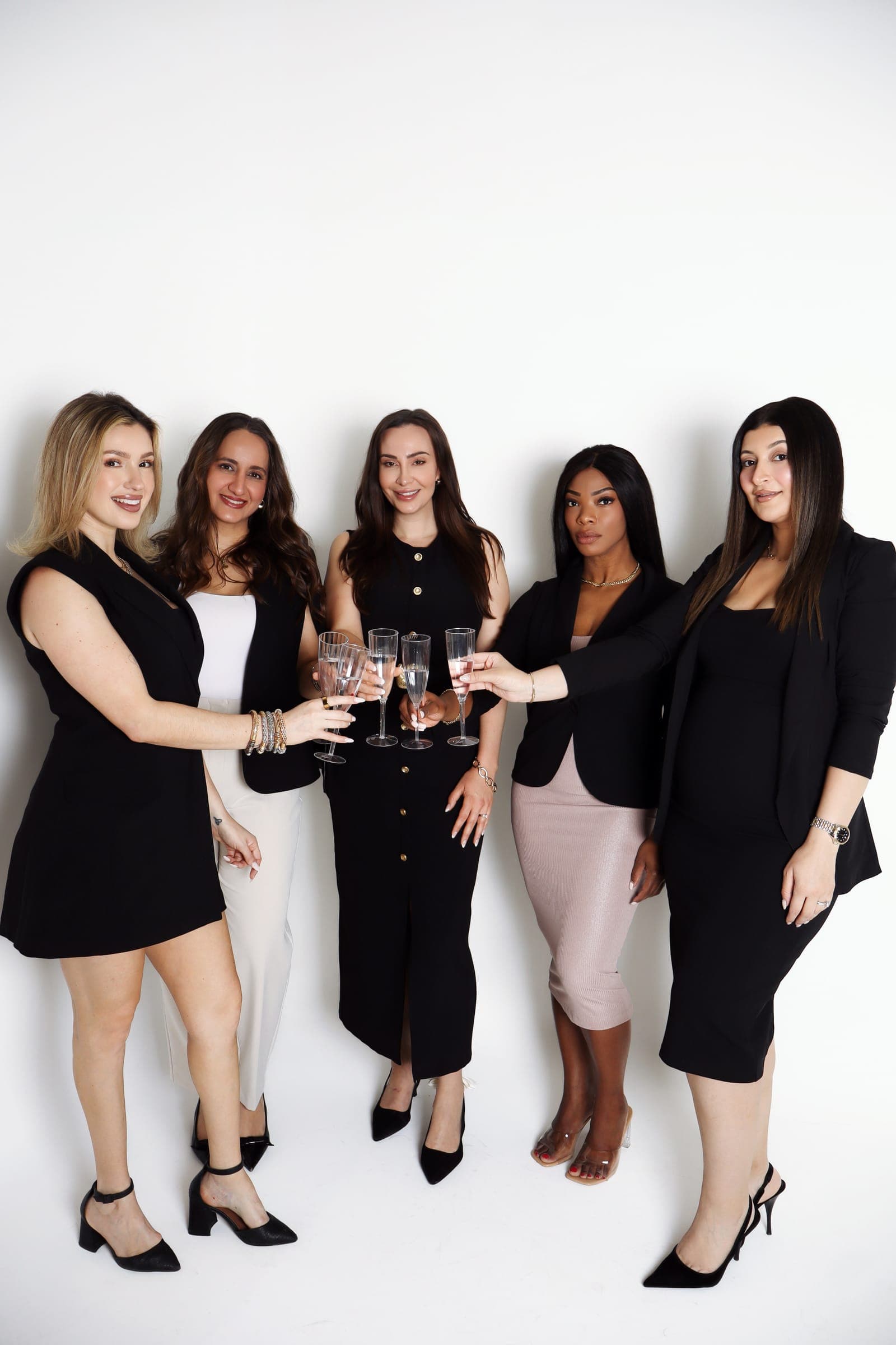 Five agents in black and blush outfits toasting with champagne flutes, photographed from above
