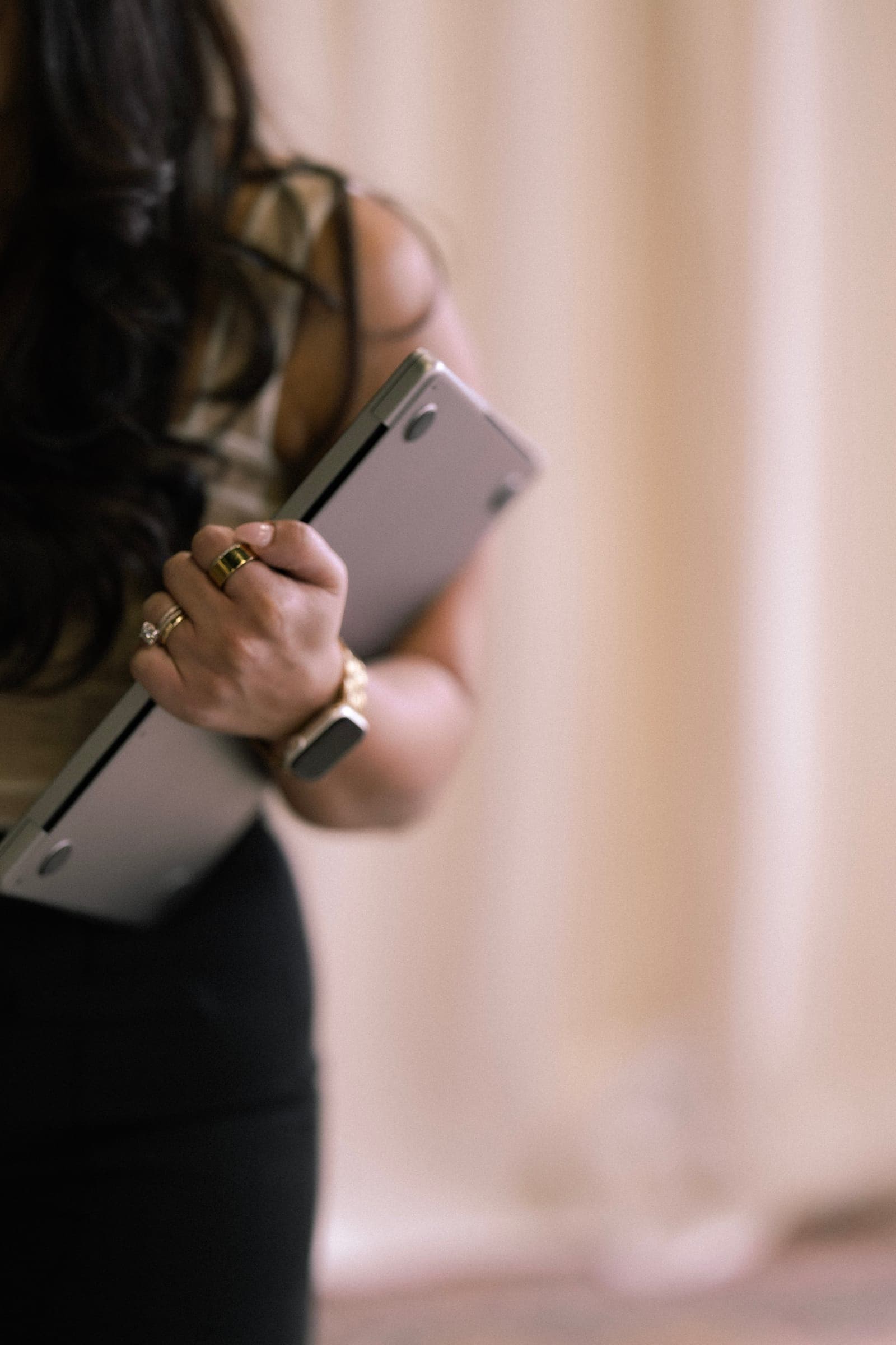 An agent holding a laptop against her side, face turned away, against a cream curtain
