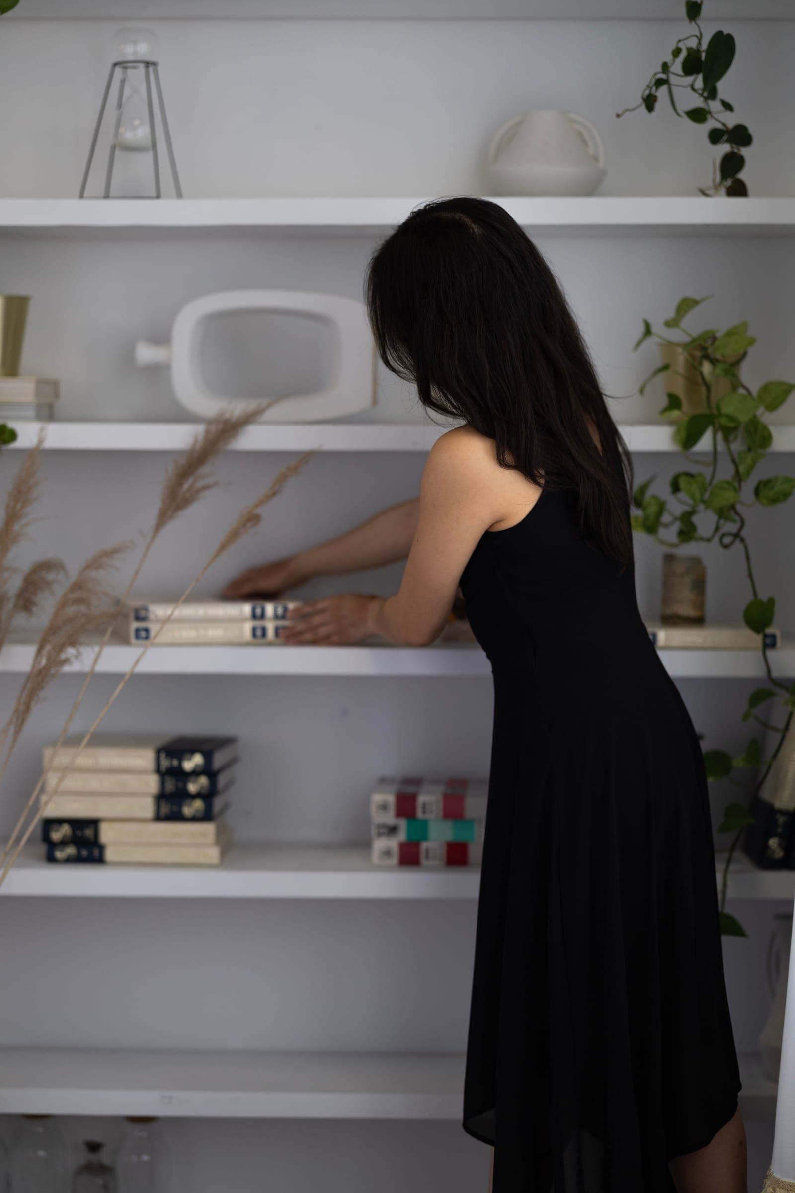 An agent styling the shelves of the studio, reaching up to arrange books and decor