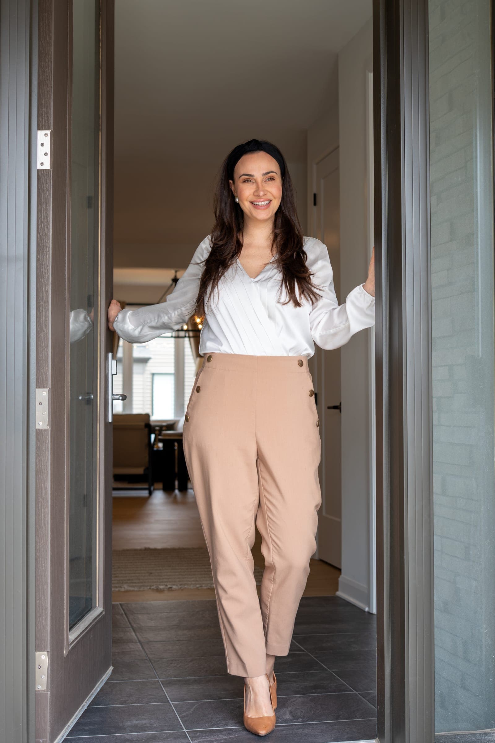 An agent standing in the open front doorway of a home, smiling at the camera