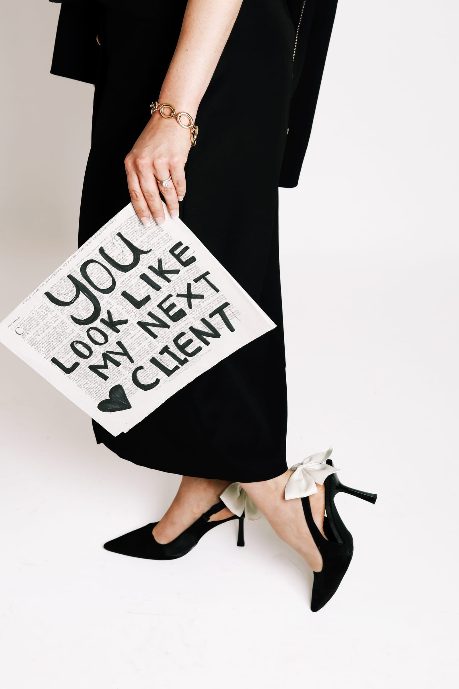 An agent in a long black skirt and heels holding a sign that reads "You look like my next client"